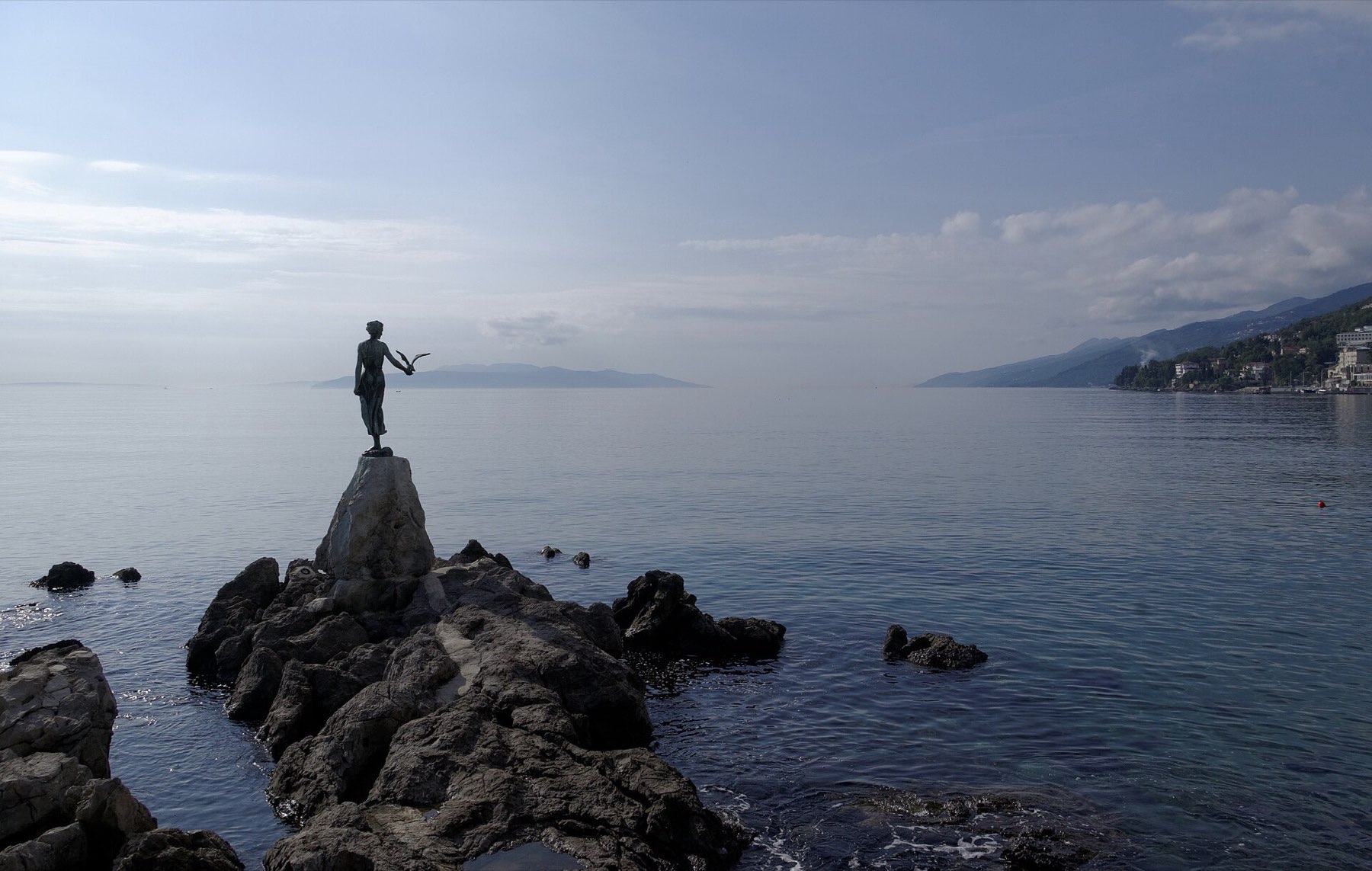 The Maiden with the Seagull statue on its seafront rock in Opatija, waves breaking behind
